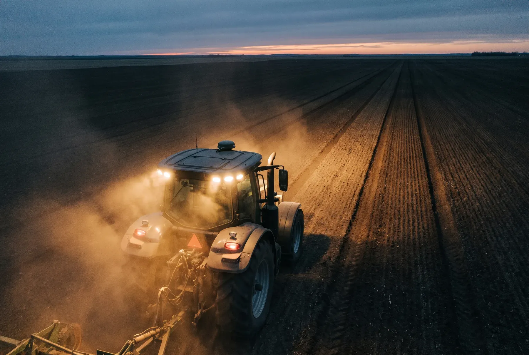 A tractor at dusk leaving parallel tracks across a field
